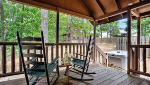 Une terrasse en bois avec des fauteuils à bascule et une table, donnant sur une zone boisée.