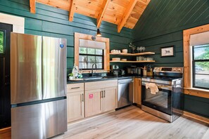A kitchen with stainless steel appliances, wooden cabinets, and a window with a view of greenery. - Pet-Friendly Cabin Near Dollywood, Hot Tub, Arcade (Sevierville)