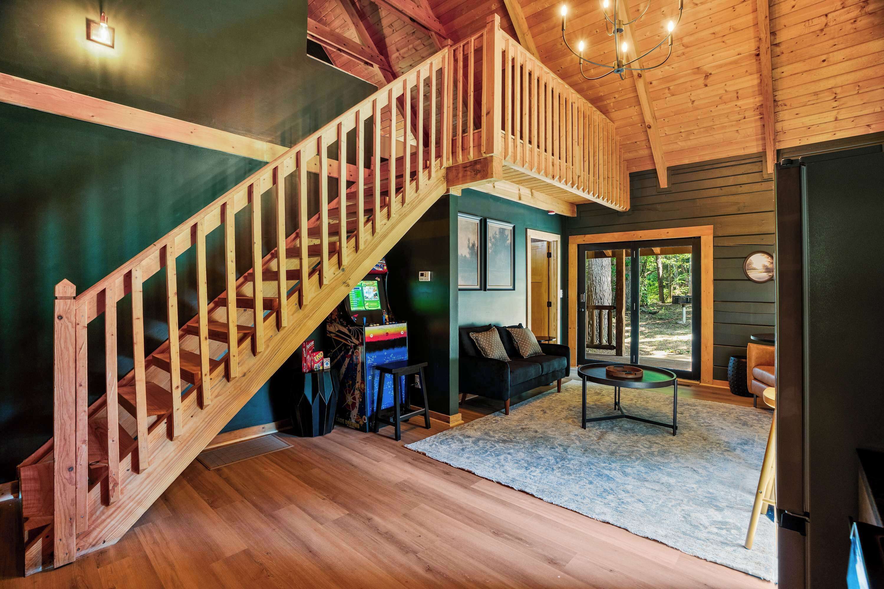 A wooden staircase leading to a loft, a dark green wall, a black sofa, a small round table, and a door leading outside.