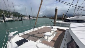 A boat deck with seating, a table, and a view of the marina and hills. - Sun-Kissed Sailing Adventure in Gran Barrera de Coral from Playa Airlie, Queensland (Airlie Beach)