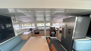 A compact kitchen with a central island, seating area with blue cushions, and a refrigerator. - Sun-Kissed Sailing Adventure in Gran Barrera de Coral from Playa Airlie, Queensland (Airlie Beach)
