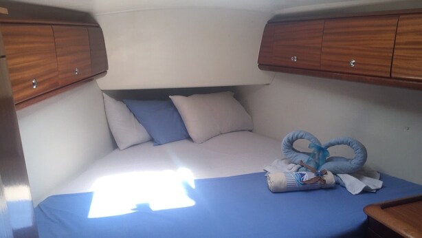 Una cama pequeña con una colcha azul, dos almohadas y una toalla enrollada.