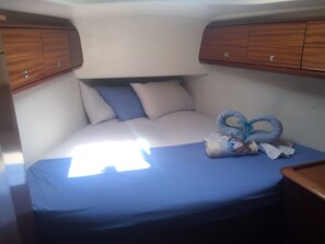 Ein kleines Bett mit blauer Bettdecke, zwei Kissen und einem zusammengerollten Handtuch.