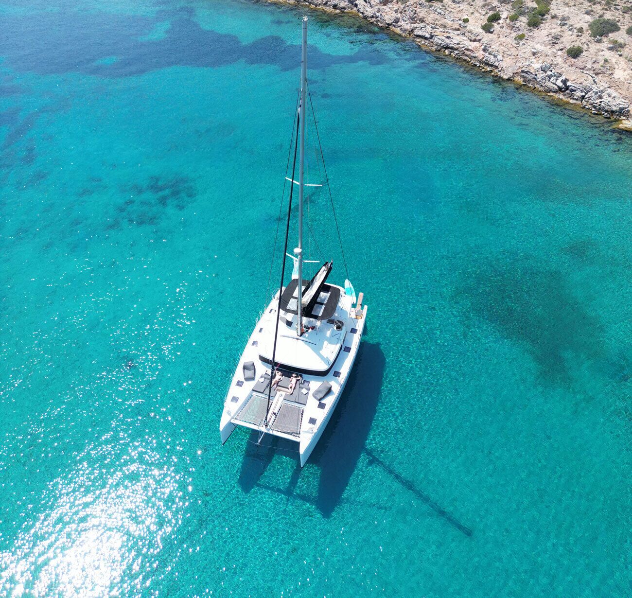 Ein Segelboot im kühlen, türkisblauen Wasser vor einer felsigen Küste.