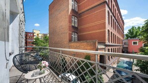 Un balcon avec des meubles d’extérieur, une voiture blanche et, au fond, un bâtiment en briques rouges.