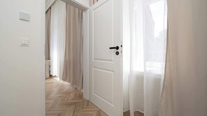 Un couloir doté d’un parquet en bois disposé en chevrons, d’une porte blanche avec une poignée noire et d’un interrupteur sur le mur.