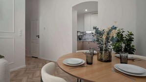 Un coin repas avec une table ronde, de l’assiette blanche, des couverts et un vase avec des plantes.