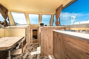 Eine kleine Kombüze mit Holztisch, einer kompakten Küchenzeile und einem Fenster mit Meerblick.