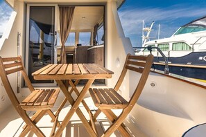 Una terraza con mesa y sillas de madera, una puerta corredera y vista a un puerto deportivo con barcos.