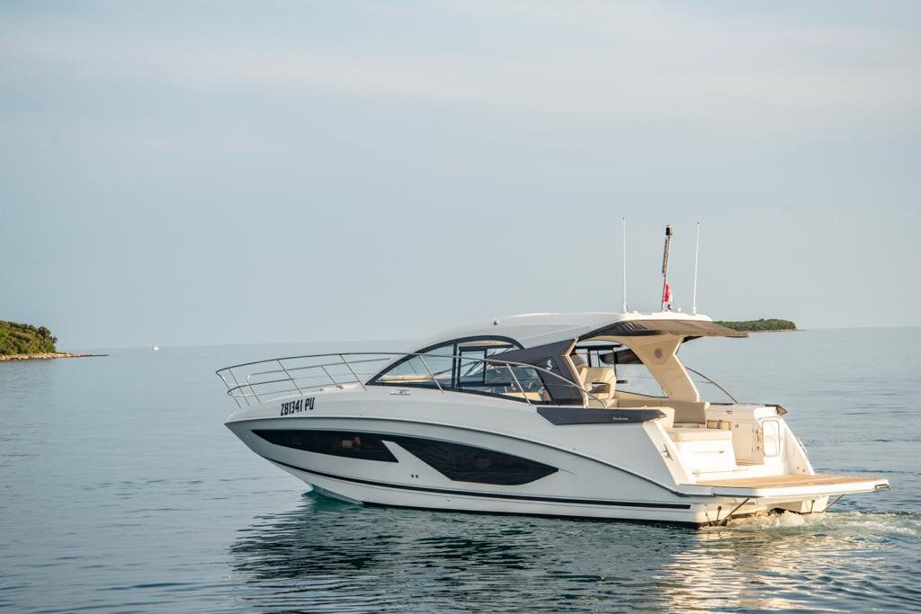 A white yacht with a cabin and a flag on top, sailing on calm waters.