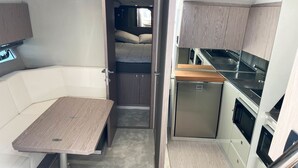 Interior compacto de una caravana con kitchenette, zona de comedor y espacio para dormir.