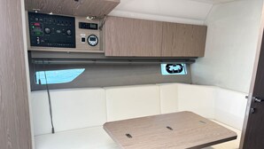 Interior de una caravana compacta, con un panel de control, zona de estar con asientos acolchados y una pequeña mesa.