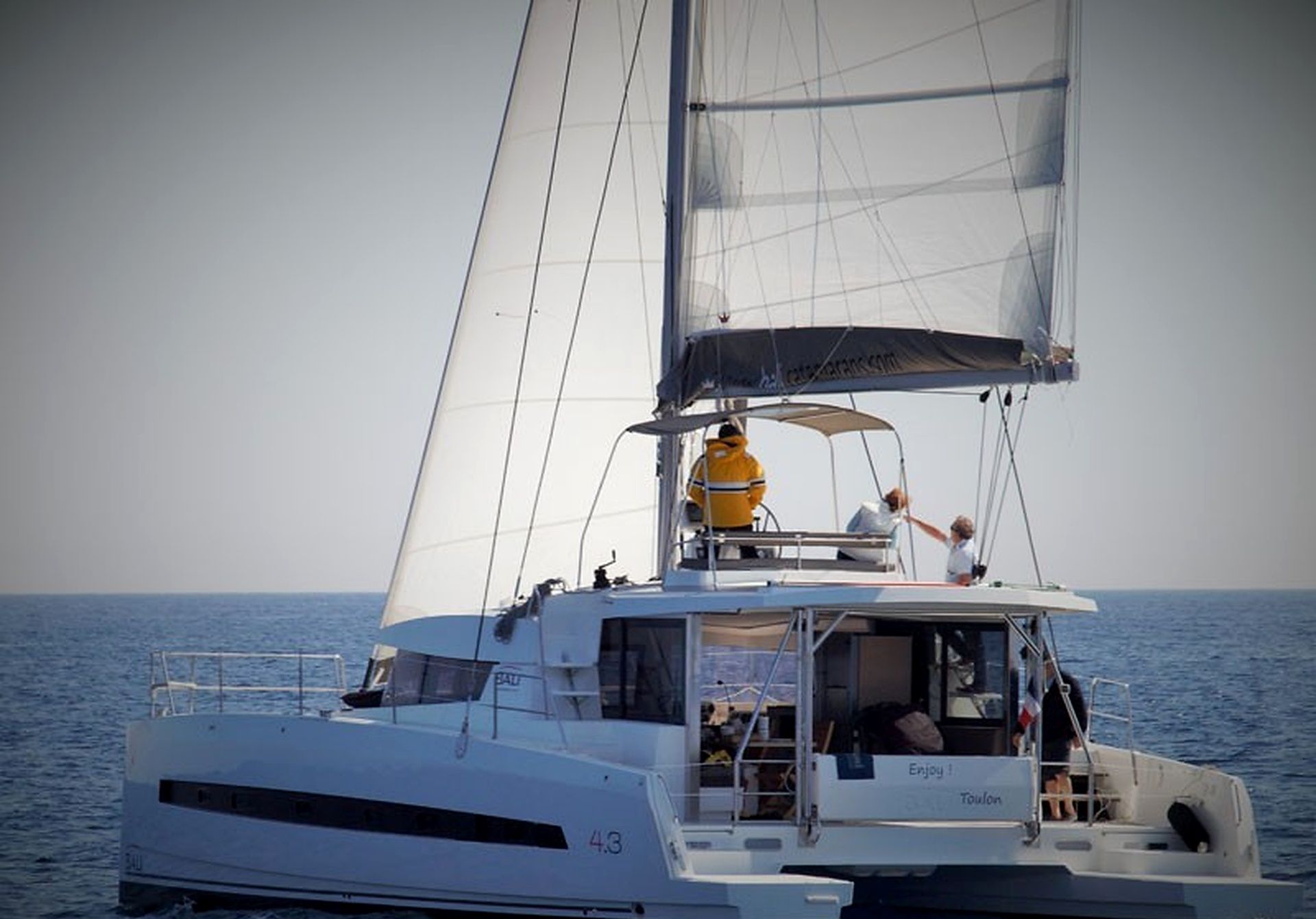 A sailboat with a cabin, a deck area, and a person wearing a yellow jacket.