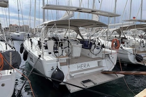 A marina with multiple sailboats docked, featuring a prominent 'HERA' name on one boat.