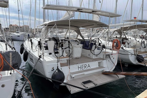 A marina with multiple sailboats docked, featuring a prominent 'HERA' name on one boat.