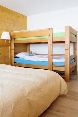 A bunk bed with a wooden headboard, a bedside lamp, and a plain wall in the background. - Graebi Appartement/Fewo, Dusche und Bad, WC 8-Bettwohnung by Interhome (Gstaad)