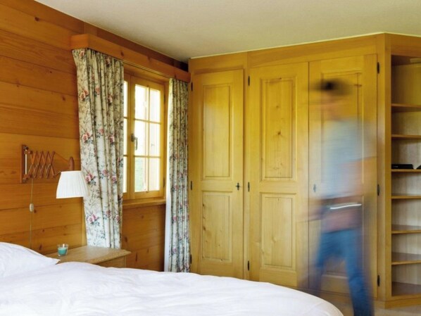 Een slaapkamer met een houten garderobe, een bed, een nachtkastje en bloemen gordijnen.