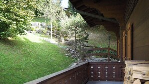 Un balcón de madera con vistas a una ladera cubierta de hierba y árboles.