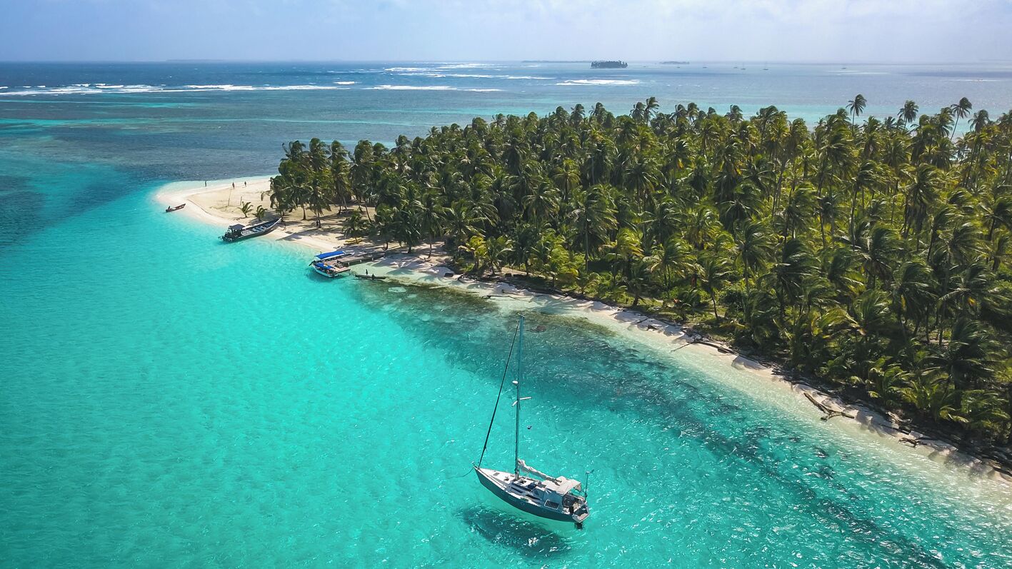 A tropical island with clear turquoise waters, a small beach, and a row of palm trees.