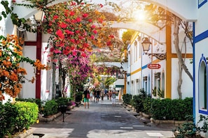 A pedestrian street lined with white buildings, a sign indicating a commercial area, and a clear sky.