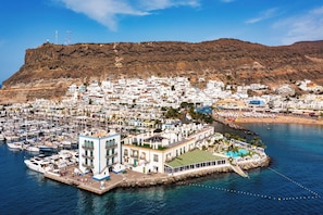 A coastal town with a marina, white buildings, and a hill in the background.