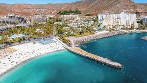 A coastal resort with a beach, a pier, and a mountainous backdrop.