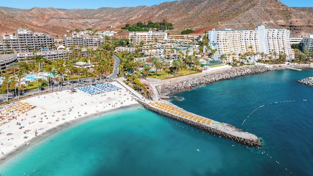 A coastal resort with a beach, a pier, and a mountainous backdrop. - Sun-Kissed Sailing Adventure in Gran Canaria, Islas Canarias (Las Palmas de Gran Canaria)
