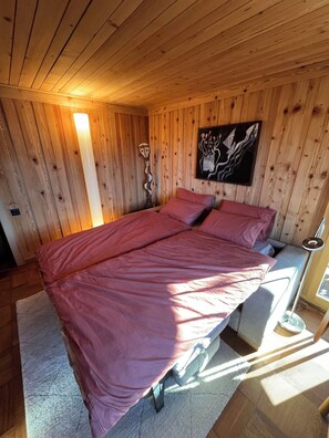 A wooden cabin bedroom with a bed, a wall-mounted artwork, and a wooden ceiling.