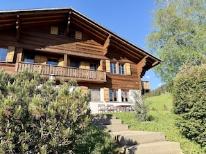 Eine Holzhütte mit Balkon, umgeben von viel Grün und blauem Himmel.