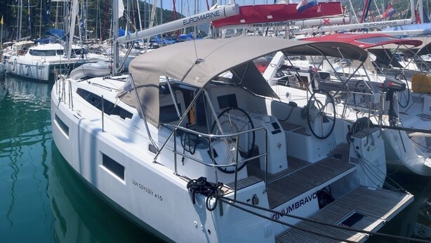 Eine weiße Yacht vom Typ SUN ODYSSEY 410 liegt in einer Marina, wo sich mehrere andere Boote befinden.