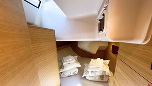 Quarto compacto e bem iluminado com cama, almofadas e uma pequena janela.