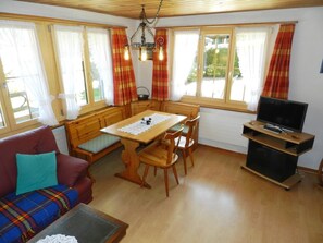 Ein gemütliches Wohnzimmer mit einer Couch, einem Esstisch mit Stühlen, einem Fernseher und einer Küchenzeile mit Fenster.