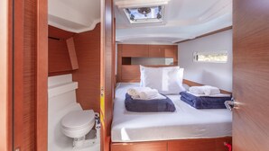 Habitación pequeña y luminosa con cama, tragaluz, inodoro y un ventanal.
