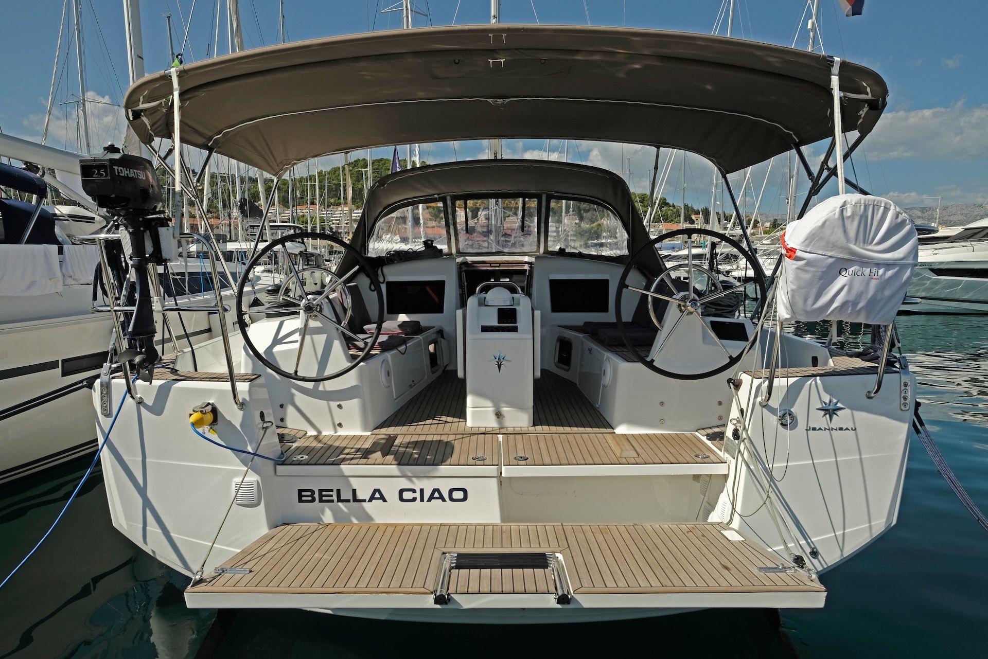 The bow of a sailboat named 'Bella Ciao' with a steering wheel, helm station, and a covered area.