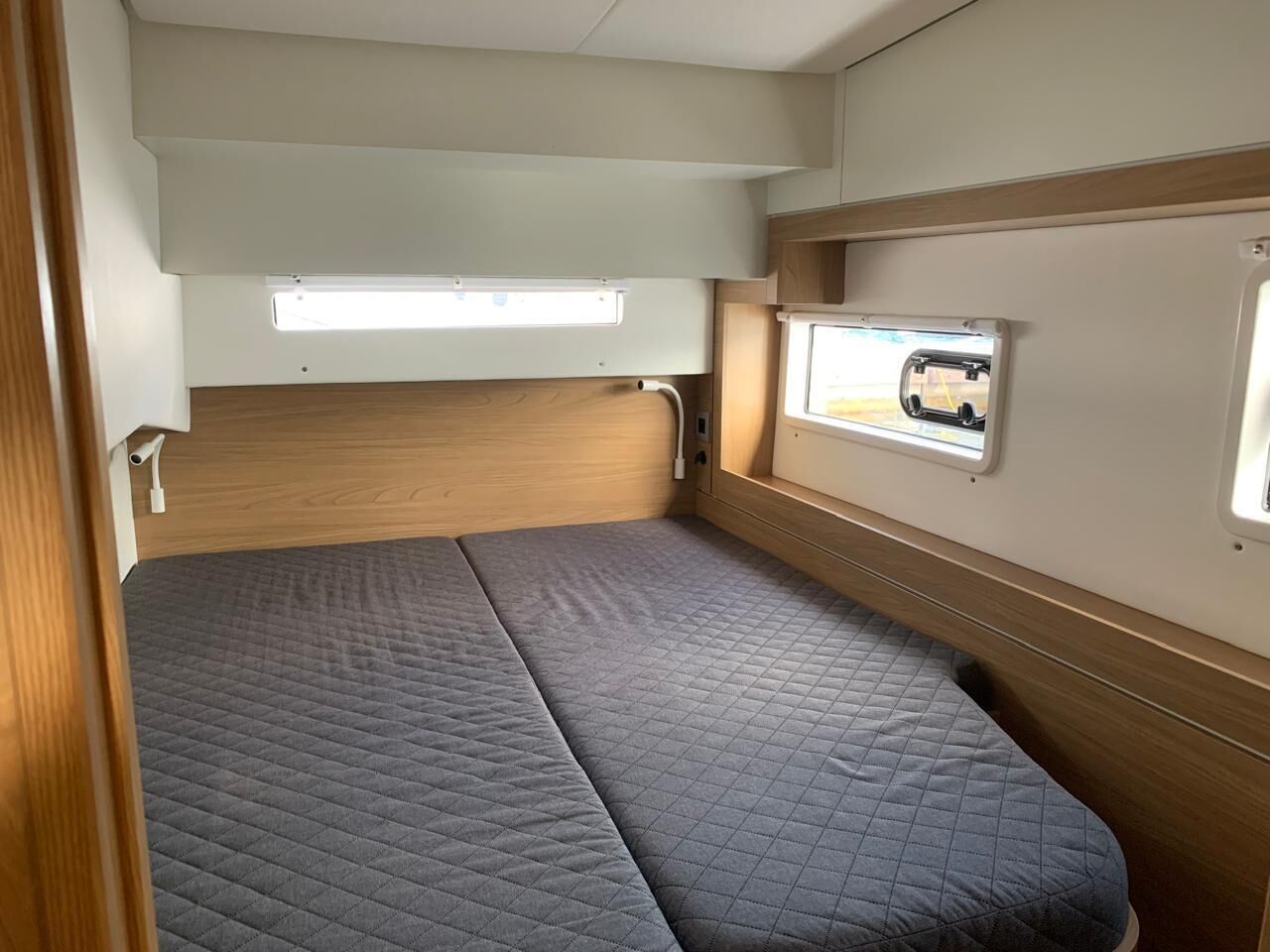 A compact RV interior with a single bed, a window, and a small kitchenette.