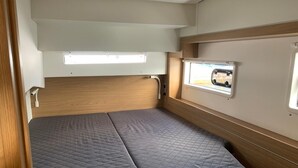 Ein kompaktes Wohnmobil-Interieur mit einem Einzelbett, einem Fenster und einer kleinen Küchenzeile.