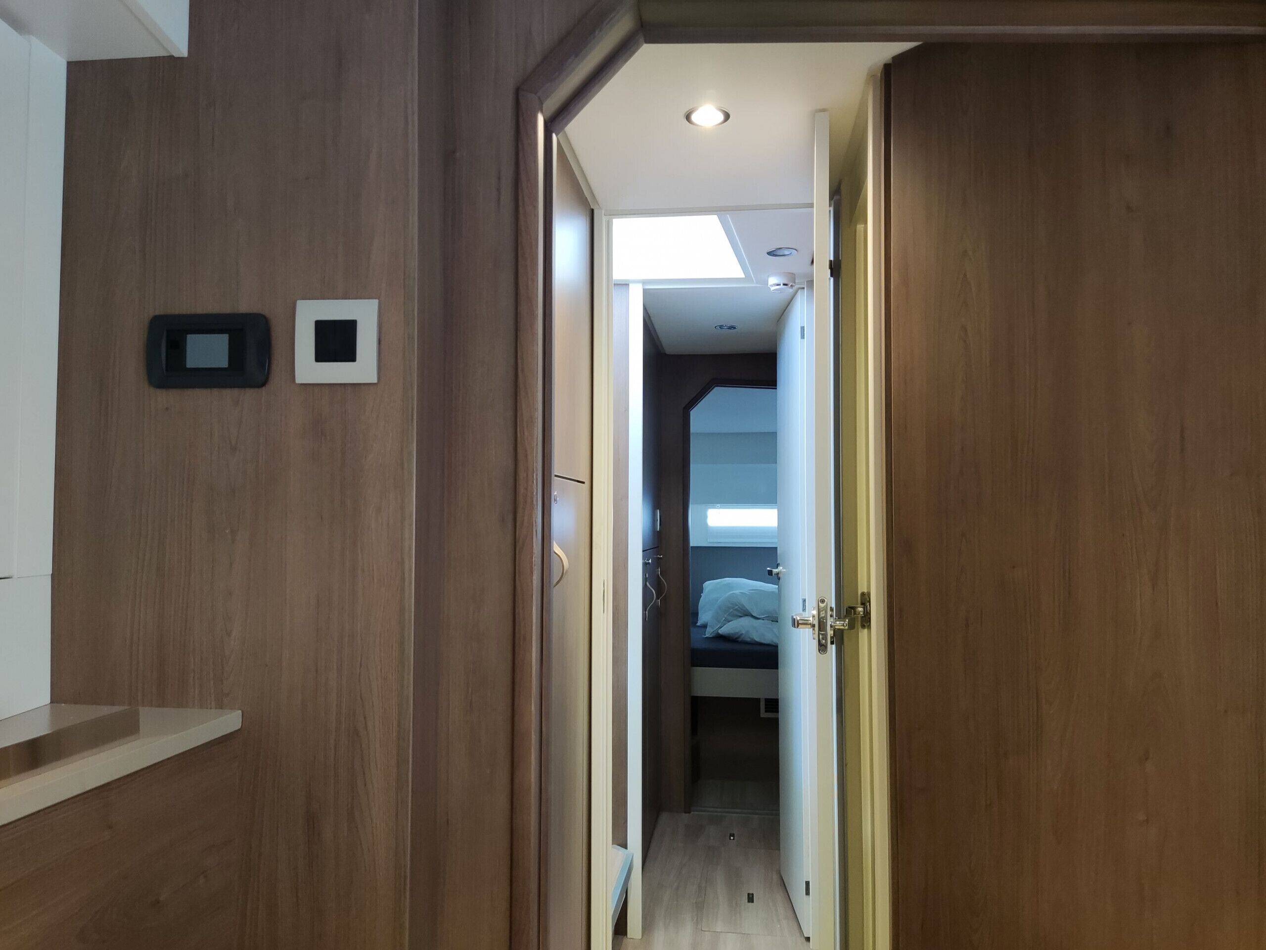 A hallway leading to a bedroom with a bed, a small window, and a door.