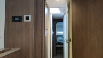 A hallway leading to a bedroom with a bed, a small window, and a door.