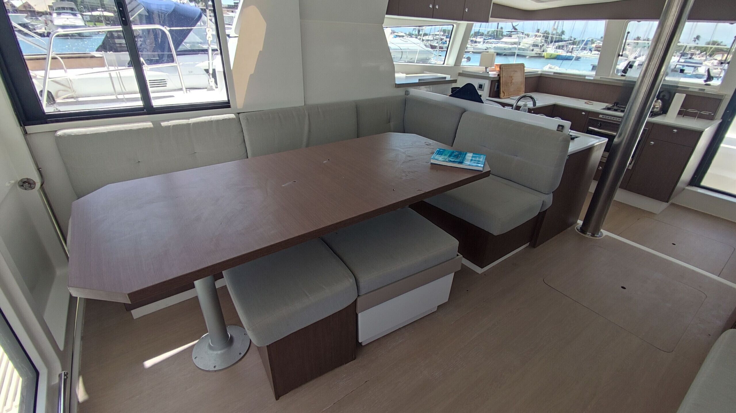 Interior de un barco con comedor, asientos acolchados y vistas al puerto deportivo.