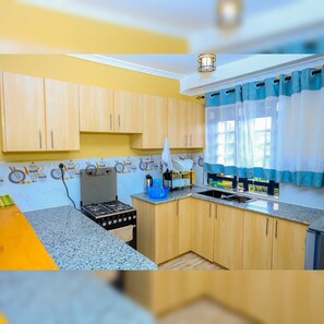 A kitchen with wooden cabinets, a gas stove, a sink, and a window with blue curtains.