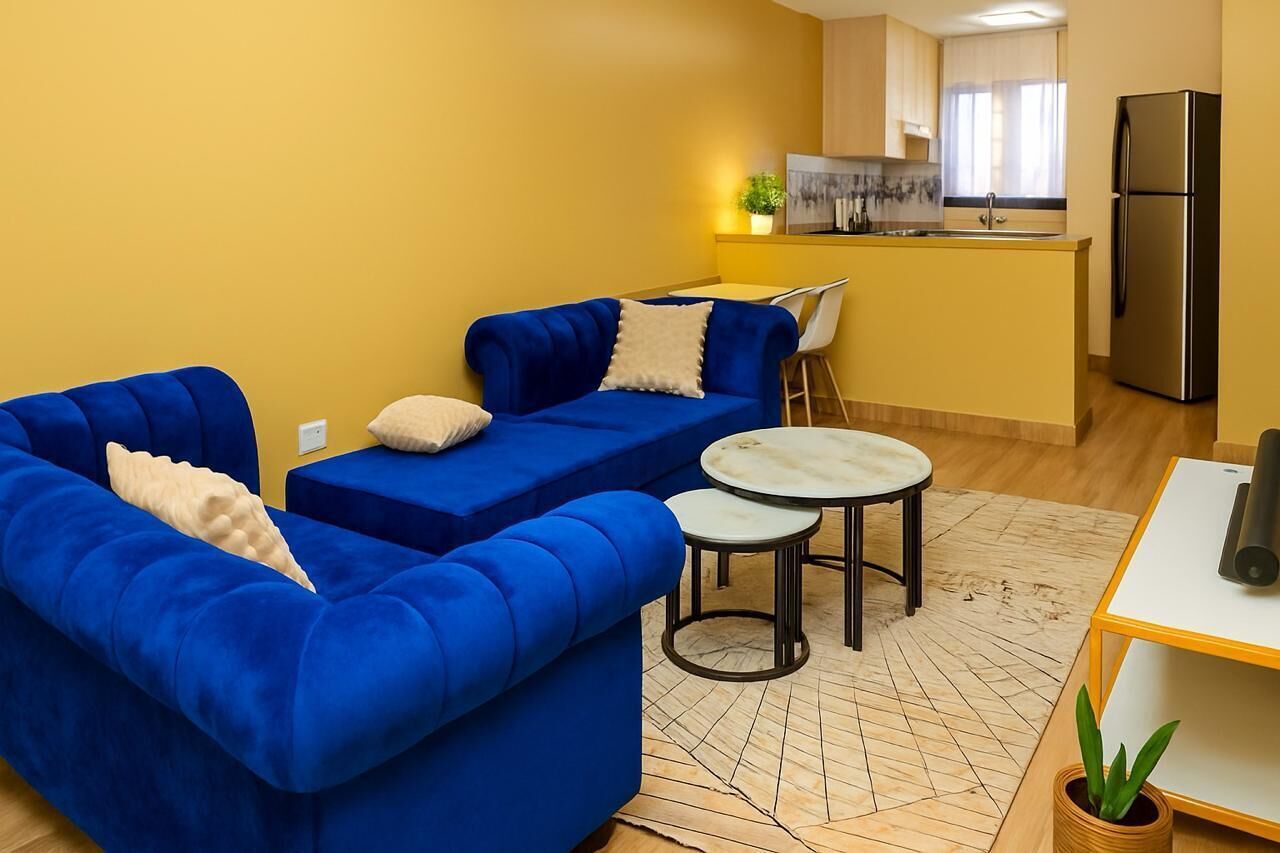 A modern living room with a blue sofa, a small round table, and a kitchen area in the background.