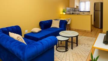 A modern living room with a blue sofa, a small round table, and a kitchen area in the background.