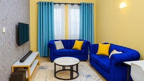 A living room with two blue sofas, a white coffee table, a flat-screen TV, and a small white table. - Cozy, secure home stay with modern comforts and a convenient location. (Kisii County)