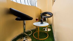 A small room with a yellow wall, a black chair, a round table with a bottle and glass, and a window with a metal railing. - Cozy, secure home stay with modern comforts and a convenient location. (Kisii County)