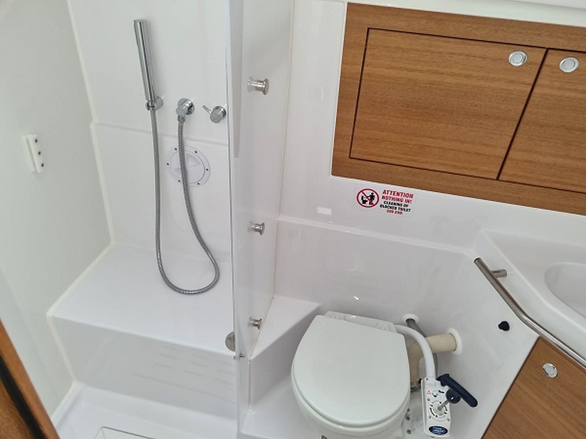 A compact bathroom with a shower, toilet, and a wooden cabinet.