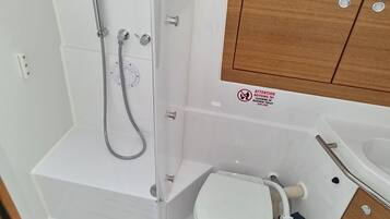 A compact bathroom with a shower, toilet, and a wooden cabinet.