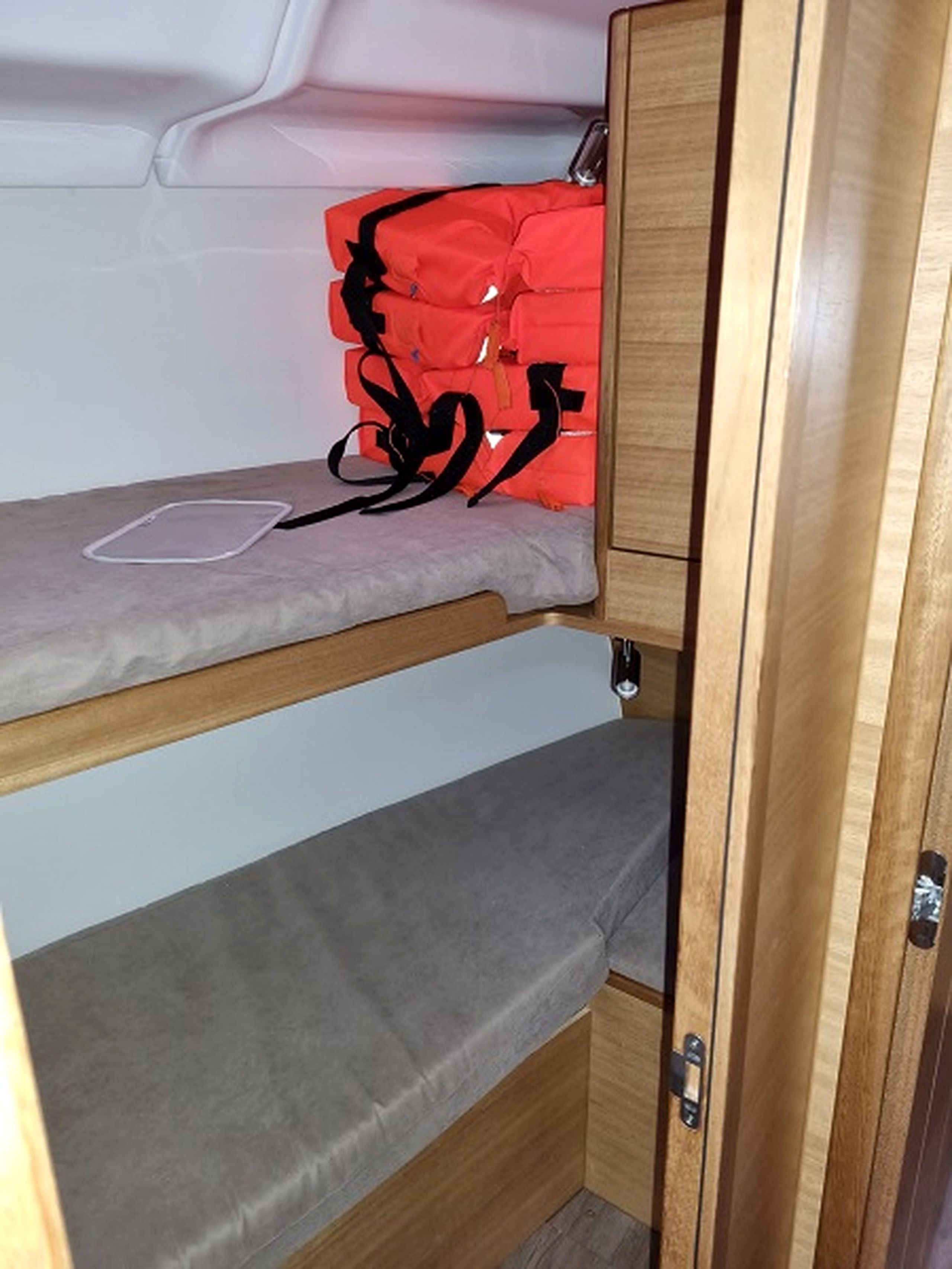 A bunk bed with a grey mattress and a red bag on the top bunk.