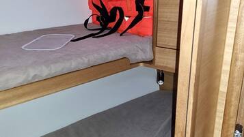 A bunk bed with a grey mattress and a red bag on the top bunk.