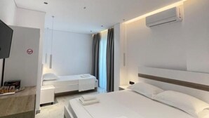 Habitación de hotel moderna con una cama grande, una cama más pequeña, un televisor y aire acondicionado instalado en la pared.