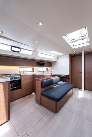 A compact galley with a stove, sink, and storage cabinets, a bench with cushions, and skylights. - Sun-Kissed Sailing Adventure in the Ionian Islands, Lefkada (Lefkada)